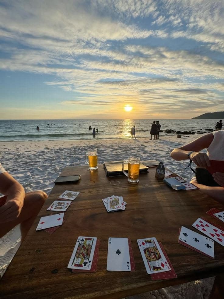 a couple playing cards on a beach at sunset